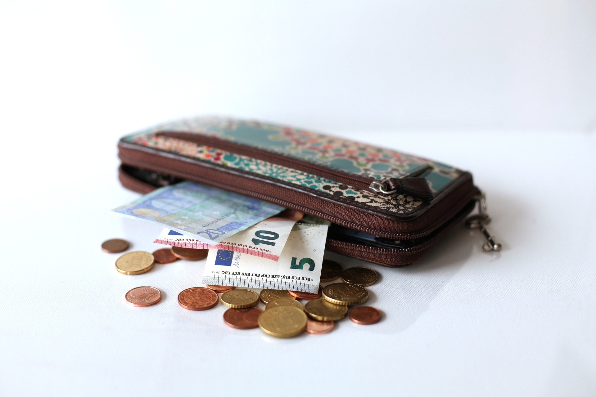 Zu sehen ist ein Portemonnaie mit einigen Euro-Scheinen und Münzen darin und daneben.