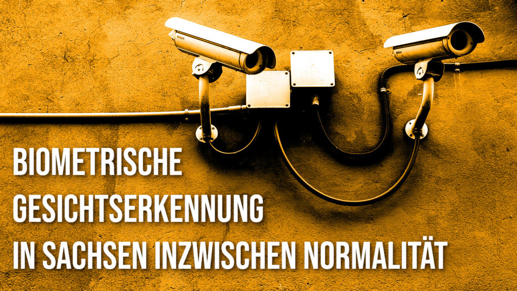 2 Überwachungskameras an einer Wand. Darunter steht: Biometrische Gesichtserkennung in Sachsen inzwischen Normalität. Das Bild ist in orange gefärbt.