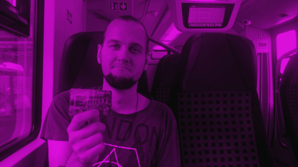 Eine Person sitzt im Zug und zeigt ein Ticket mit traurigem Gesicht nach vorn. Es ist Florian Karow.