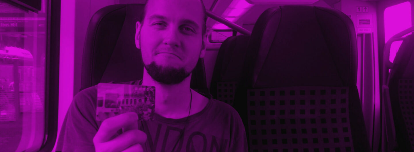 Eine Person sitzt im Zug und zeigt ein Ticket mit traurigem Gesicht nach vorn. Es ist Florian Karow.
