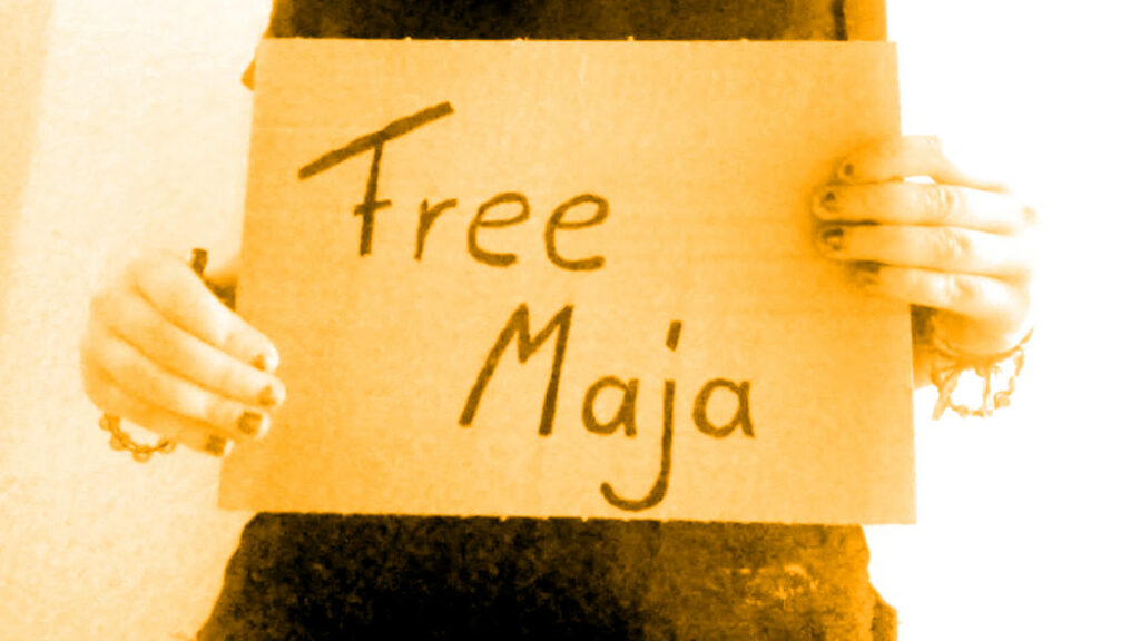 Es wird ein Pappschild gehalten. Darauf steht: "Free Maja".