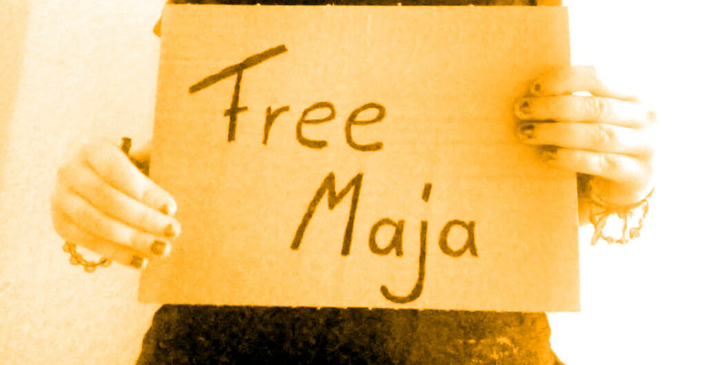 Es wird ein Pappschild gehalten. Darauf steht: "Free Maja".