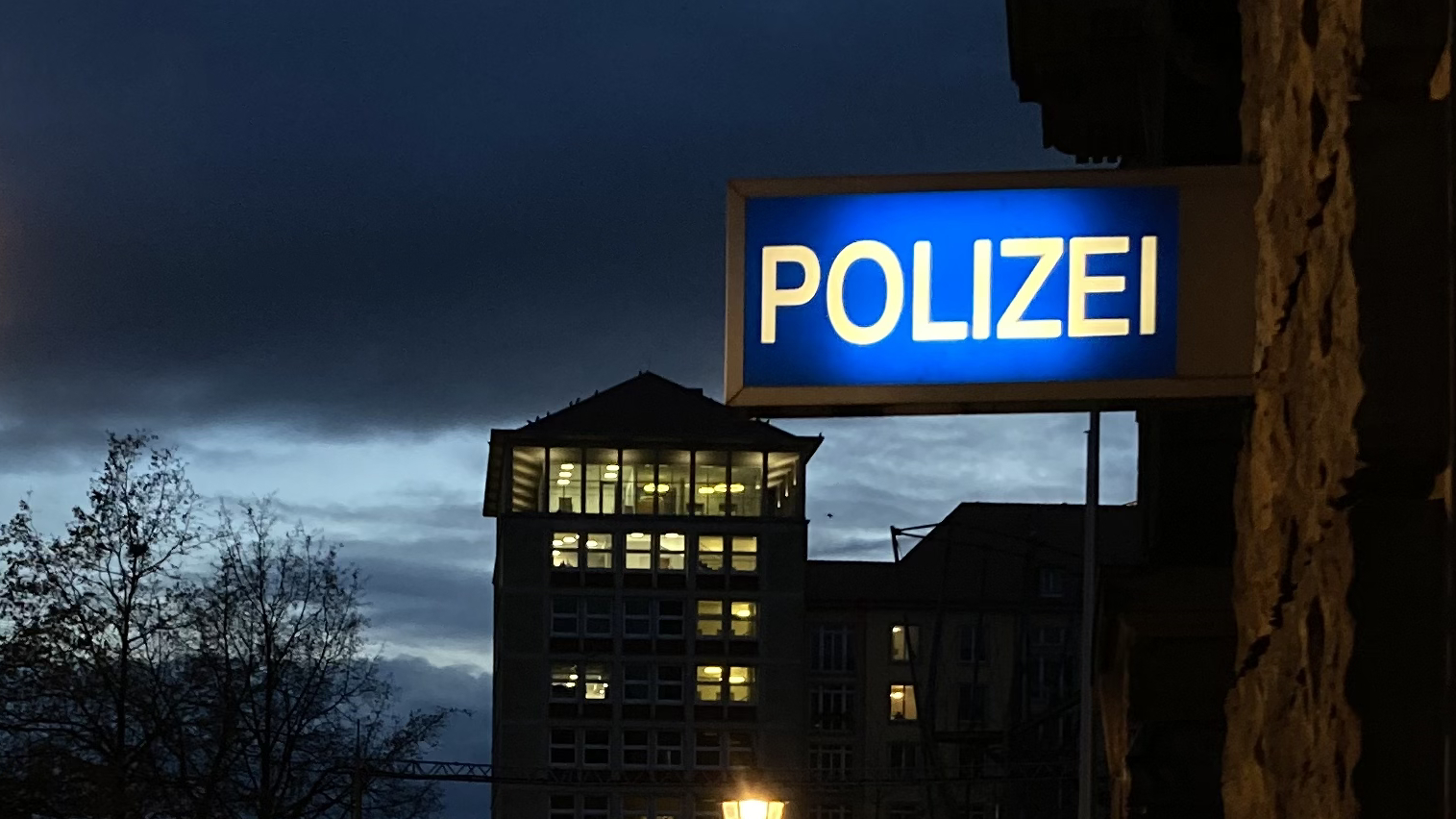 Ein beleuchtetes "Polizei"-Schild an einer Polizeiwache bei Nacht.