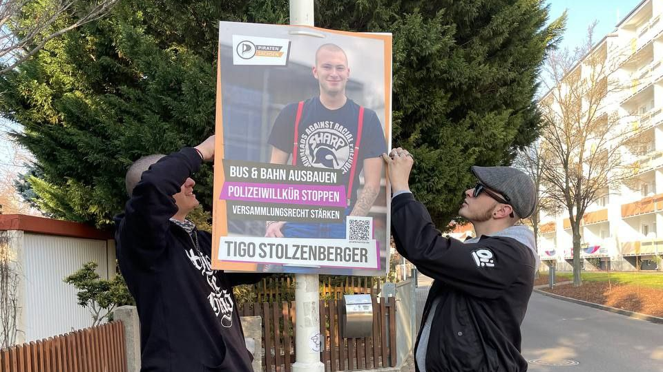 2 Personen hängen ein Wahlplakat auf.